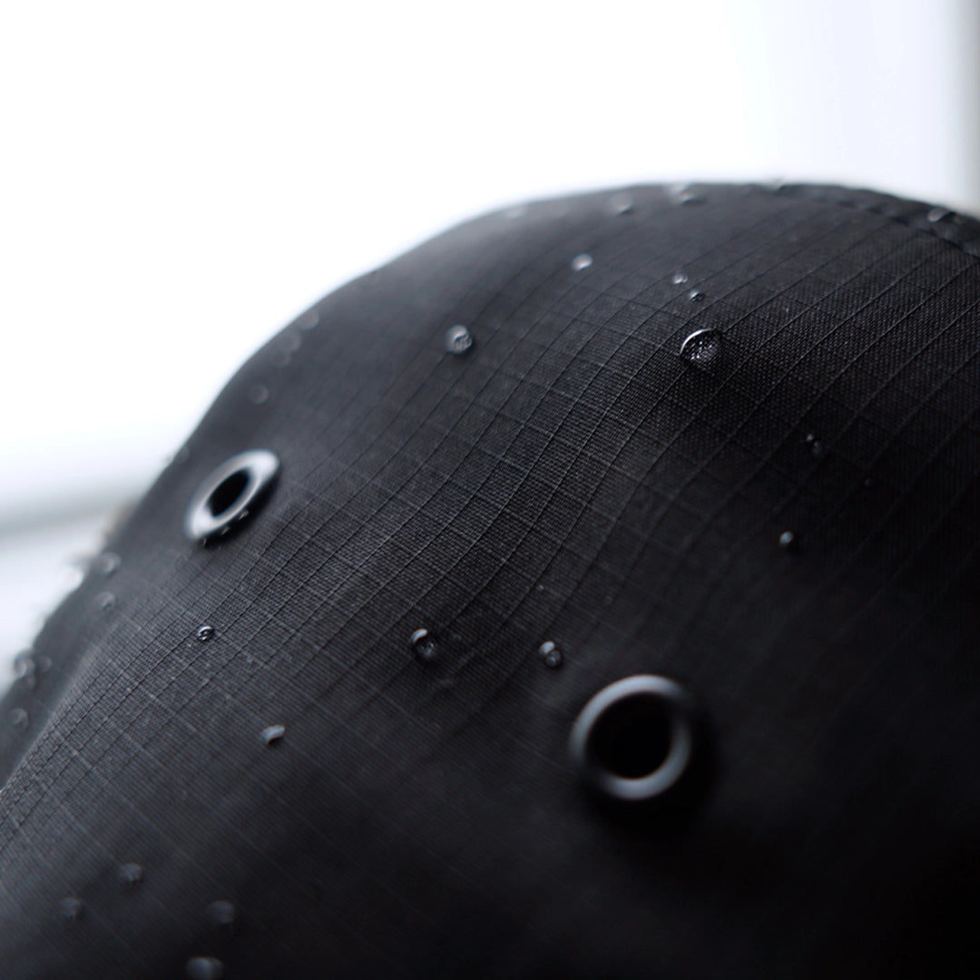 Macro close-up of the Progress Over Perfection Hat in black ripstop nylon with visible water droplets—showcasing lightweight, durable 130 GSM construction.