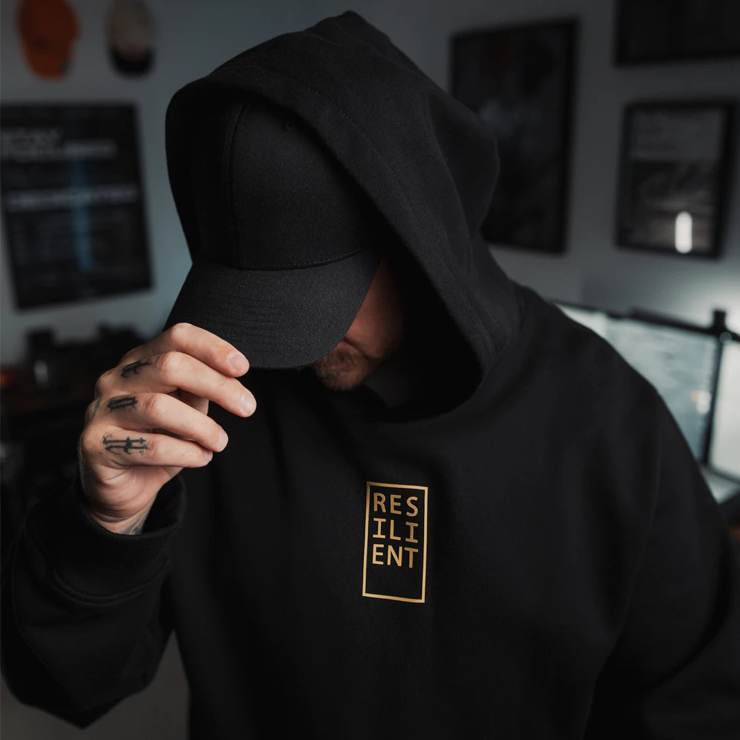 Black ODAAT hoodie featuring gold ‘RESILIENT’ box graphic — designed with a standard athletic fit for everyday movement, made from structured, sustainable cotton for comfort, resilience, and style.