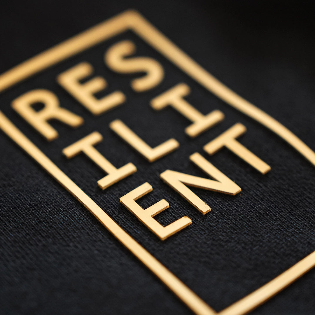 Macro close-up of the Resilient Hoodie’s raised tactile print reading ‘RESILIENT’ in a boxed layout—designed for daily, physical affirmation.