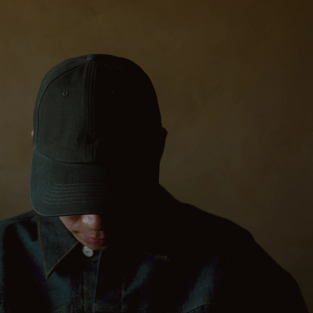 Washed black dad cap with unstructured crown and curved brim, worn with dark shirt in low light, ODAAT Signature Cap.