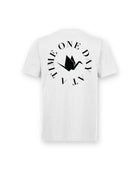 Back of Circle of Resilience Tee in Arctic White featuring a black crane emblem encircled by the phrase ‘One Day At A Time.’