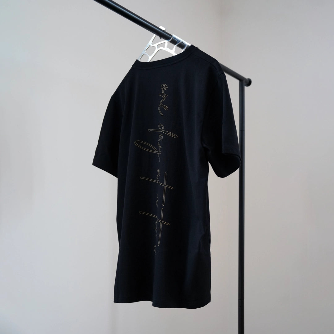 Rear view of the ODAAT Script Tee in black, featuring vertical ‘one day at a time’ script in gold ochre—designed for movement and everyday wear.