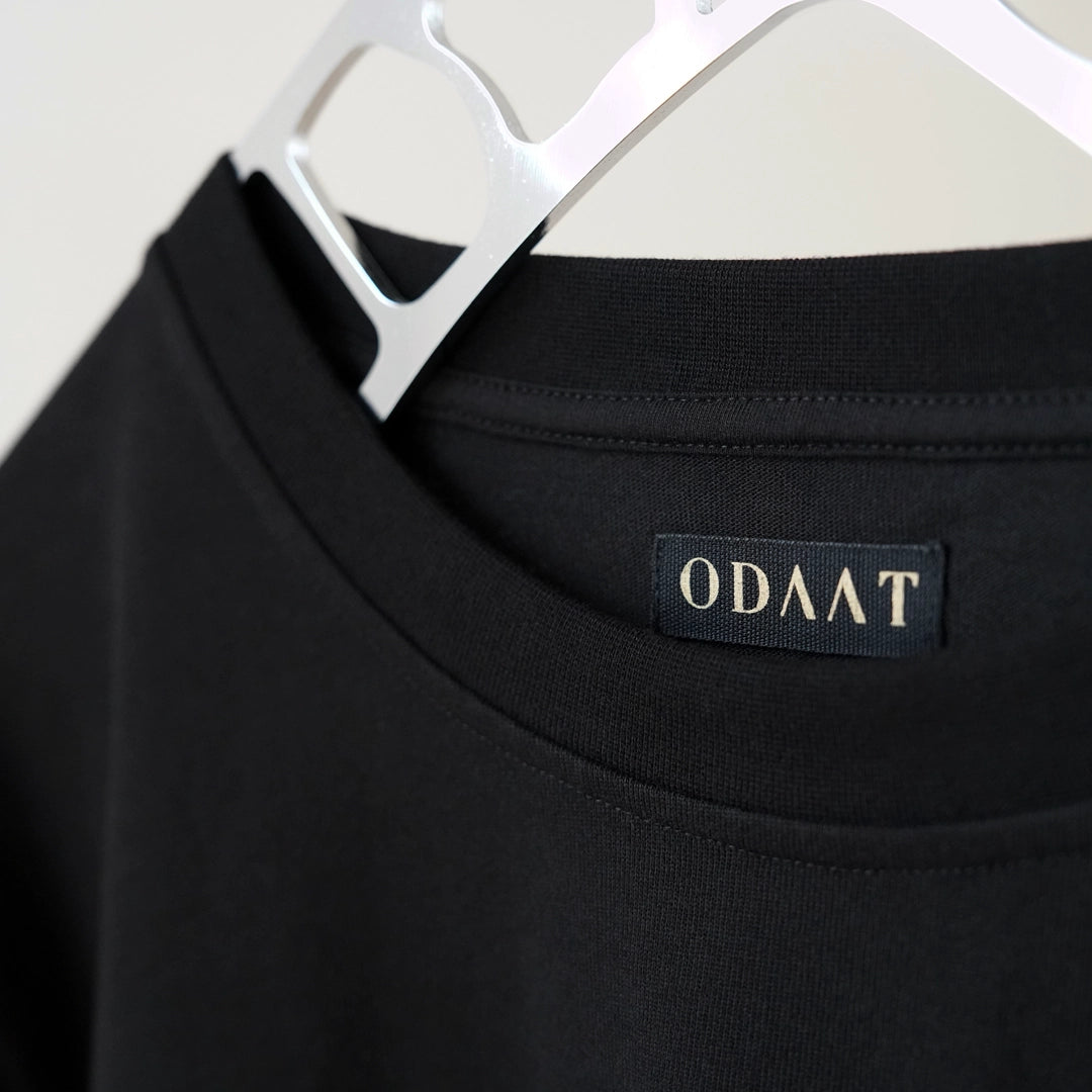 Close-up of the ODAAT neck label stitched inside the collar of the Script Tee—minimal branding with a message of progress and purpose.