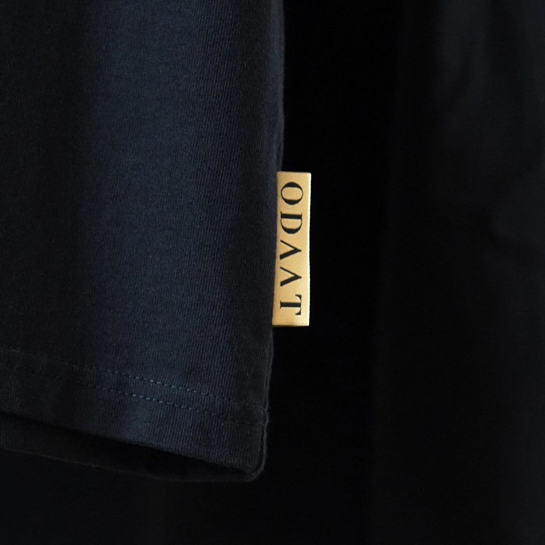 Close-up of ODAAT’s gold ochre woven label stitched into the side seam of a black tee—subtle branding that symbolizes everyday resilience.