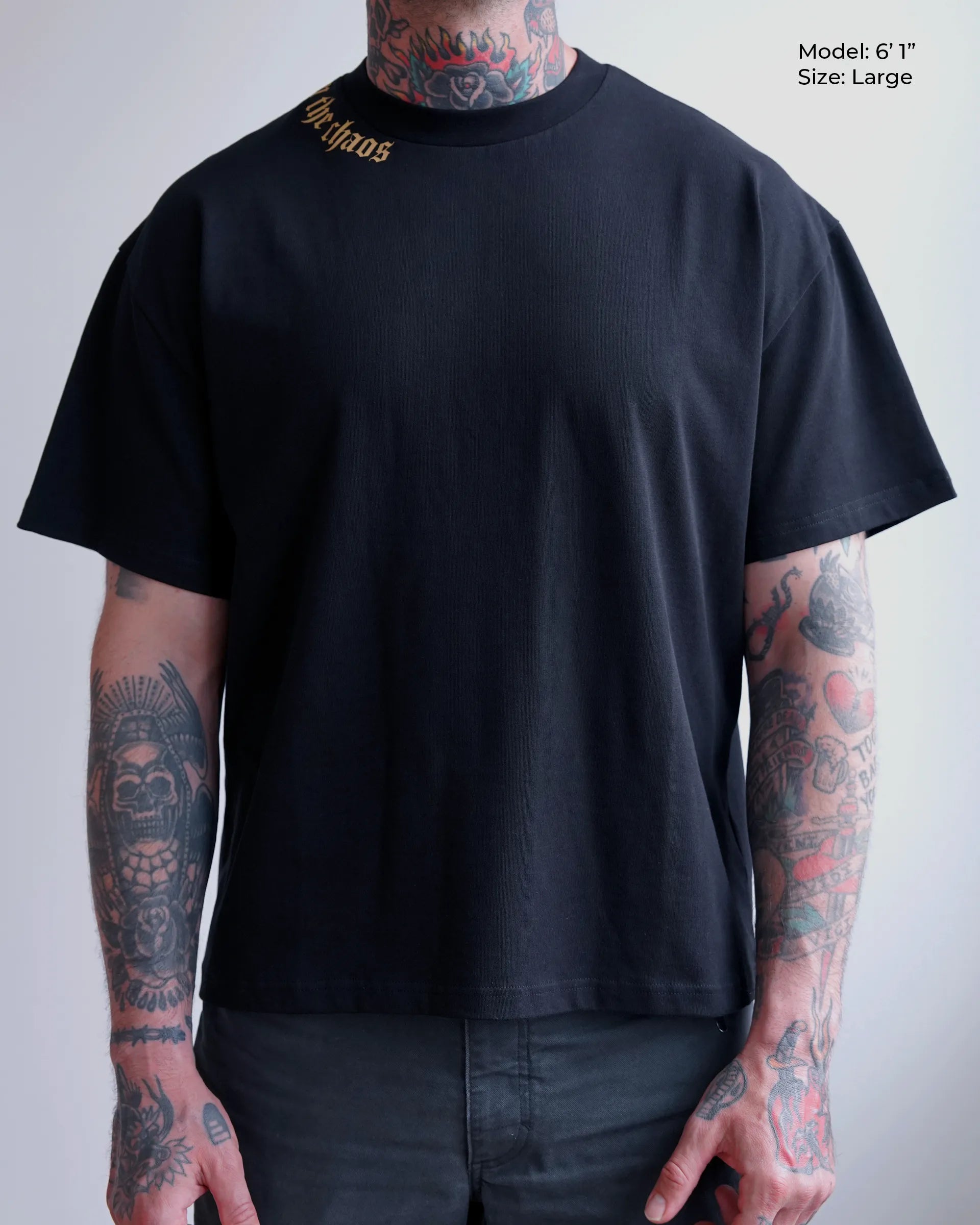 Person wearing black calm in the chaos t-shirt with visible tattoos on arms against a plain background