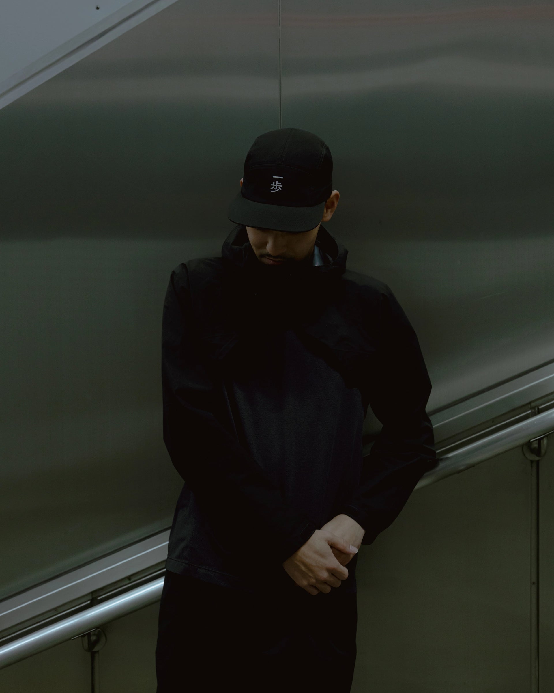 Man wearing a black KyoPace running cap with kanji mark on front in a moody indoor setting