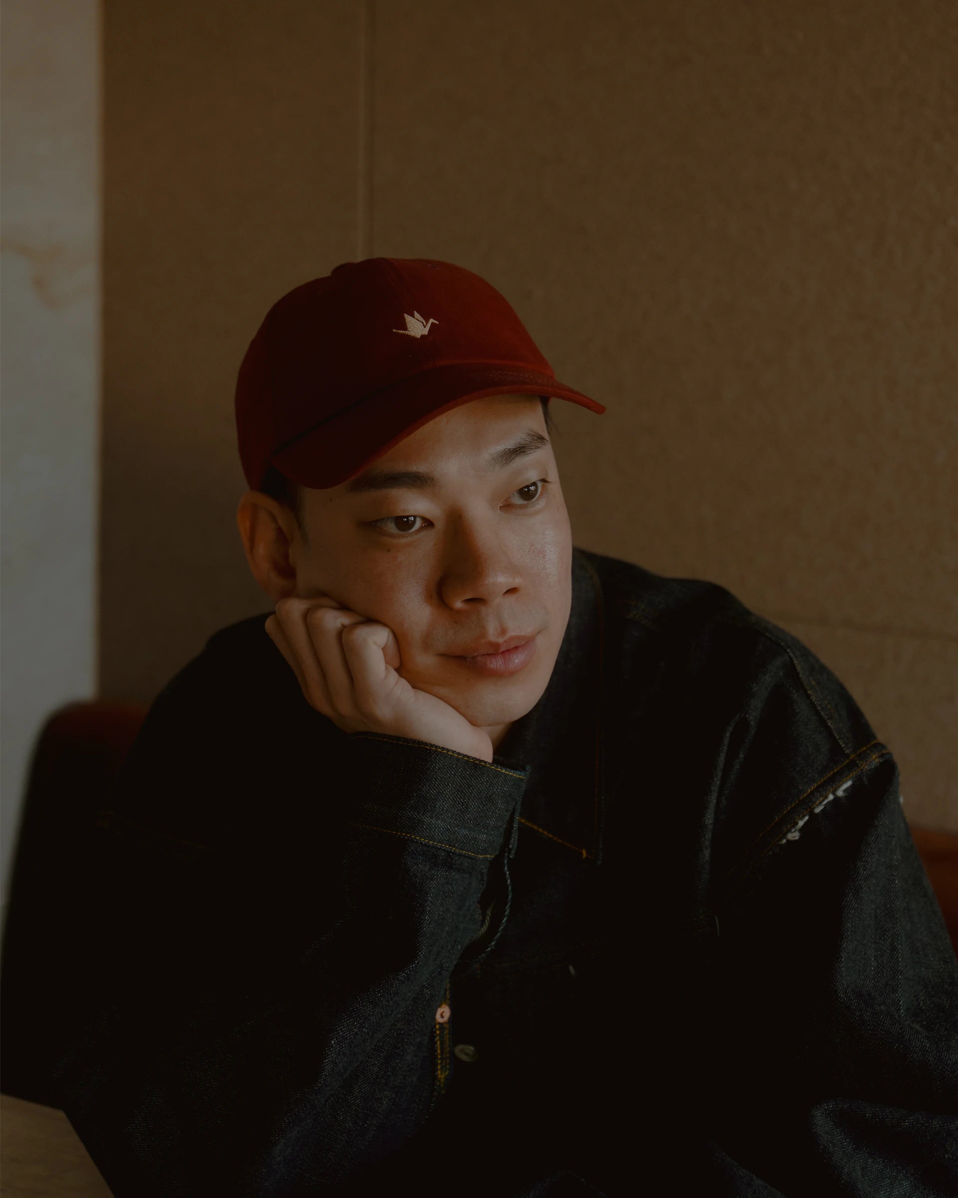 burgundy signature dad cap worn in lifestyle setting, soft cotton hat with curved brim and crane embroidery, relaxed portrait with warm tones and minimal background