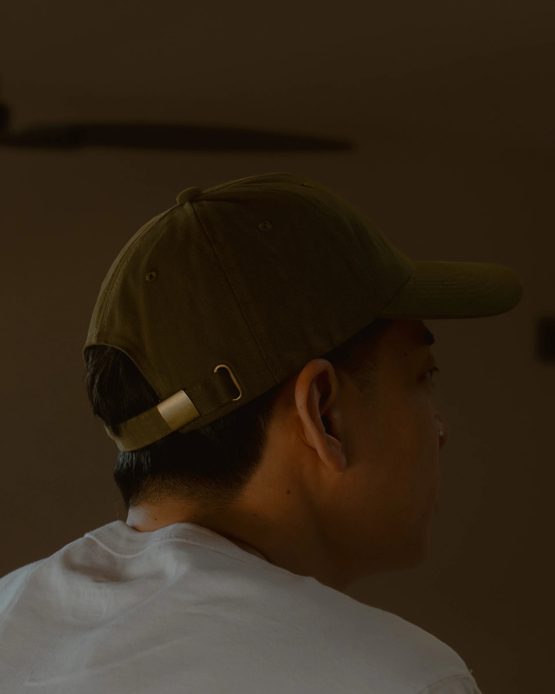 olive signature dad cap rear detail worn by model, showing self-fabric strap and metal adjuster buckle, side profile with soft cotton texture and warm indoor lighting