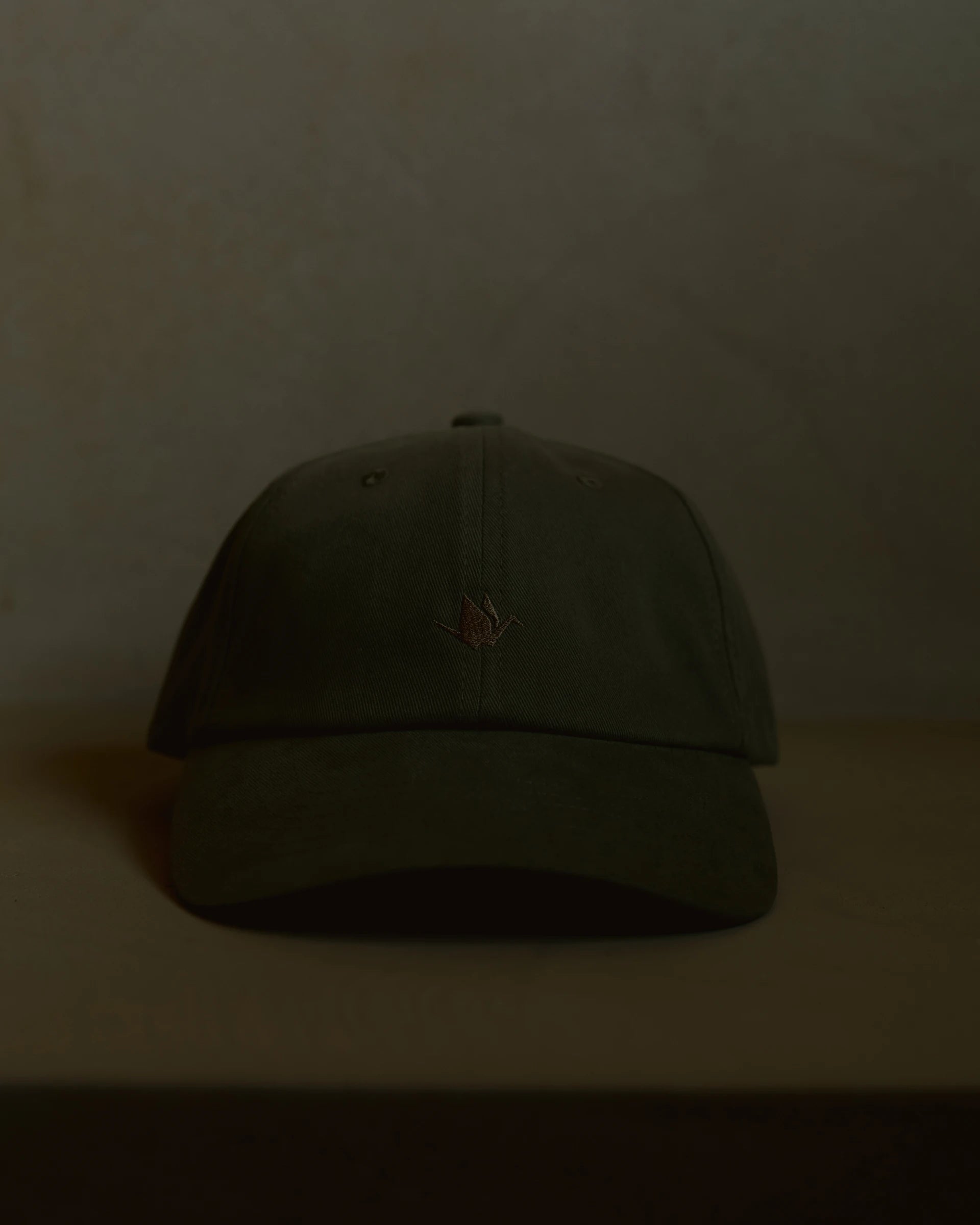olive signature dad cap front view with curved brim, structured crown and centered crane embroidery, minimal product shot on neutral surface with soft warm lighting