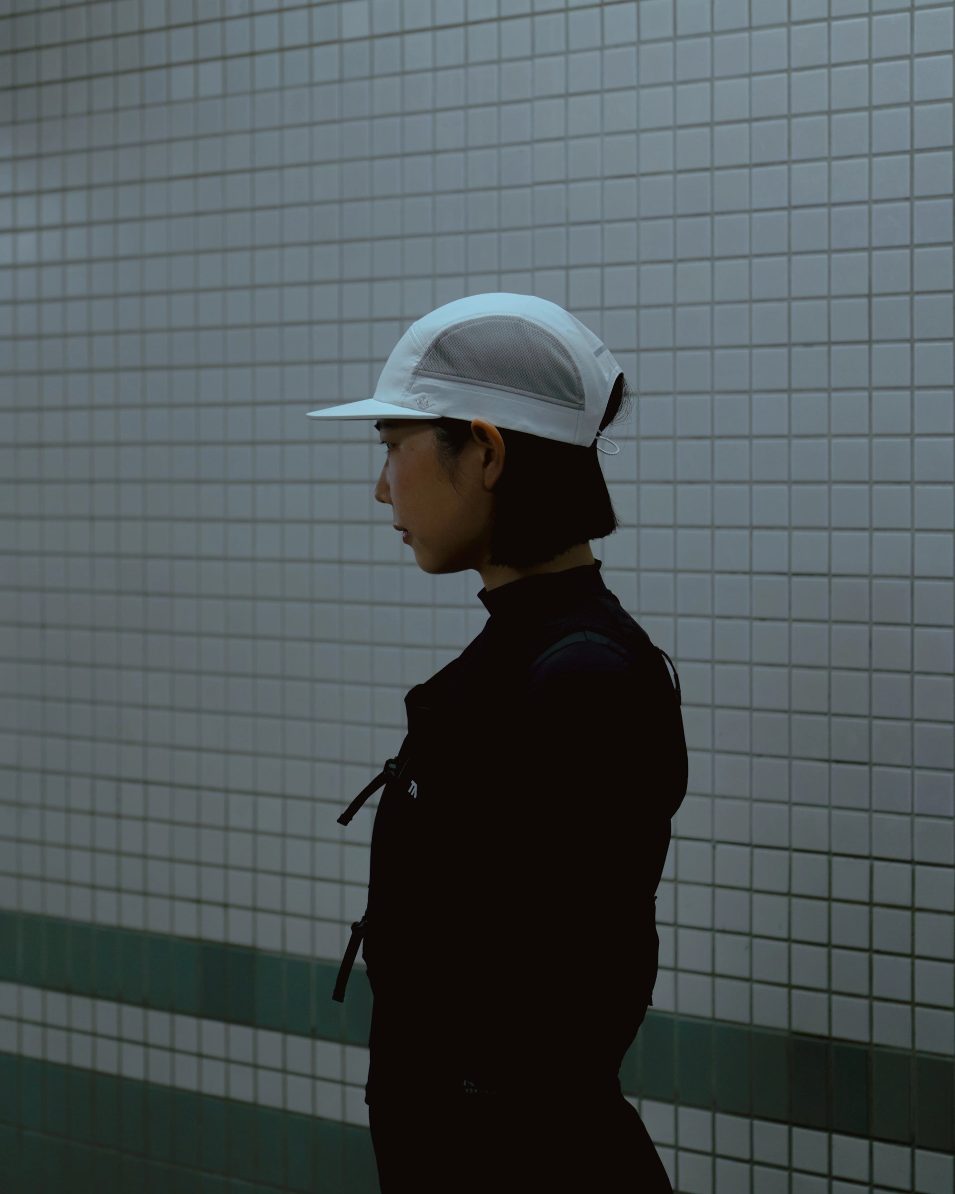 Side profile of model wearing white KyoPace running cap against tiled wall