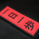 Macro close-up of the KyoPace Hoodie’s red embroidered chest patch with Japanese text reading ‘One Day, One Step,’ symbolizing steady progress.