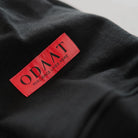Close-up of the KyoPace Hoodie’s red woven label reading ‘ODAAT – Resilience Lives Here,’ stitched onto heavyweight black fabric.
