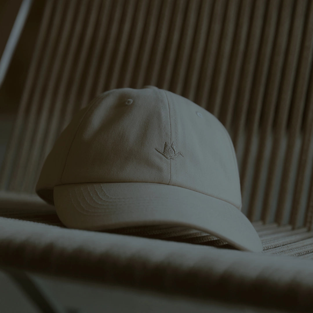 Off-white dad cap with tonal crane embroidery, brushed cotton texture and curved brim, ODAAT Signature Cap in rice paper color.
