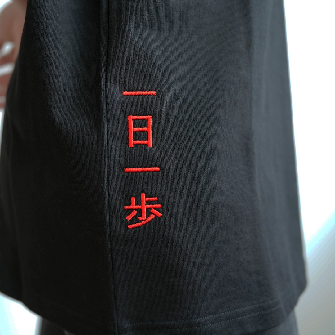 Close-up of ODAAT Apparel black t-shirt with red vertical embroidery reading ‘一日一歩’—Japanese for ‘One day, one step.’ The minimalist stitch detail represents progress and resilience, inspired by Japanese design.
