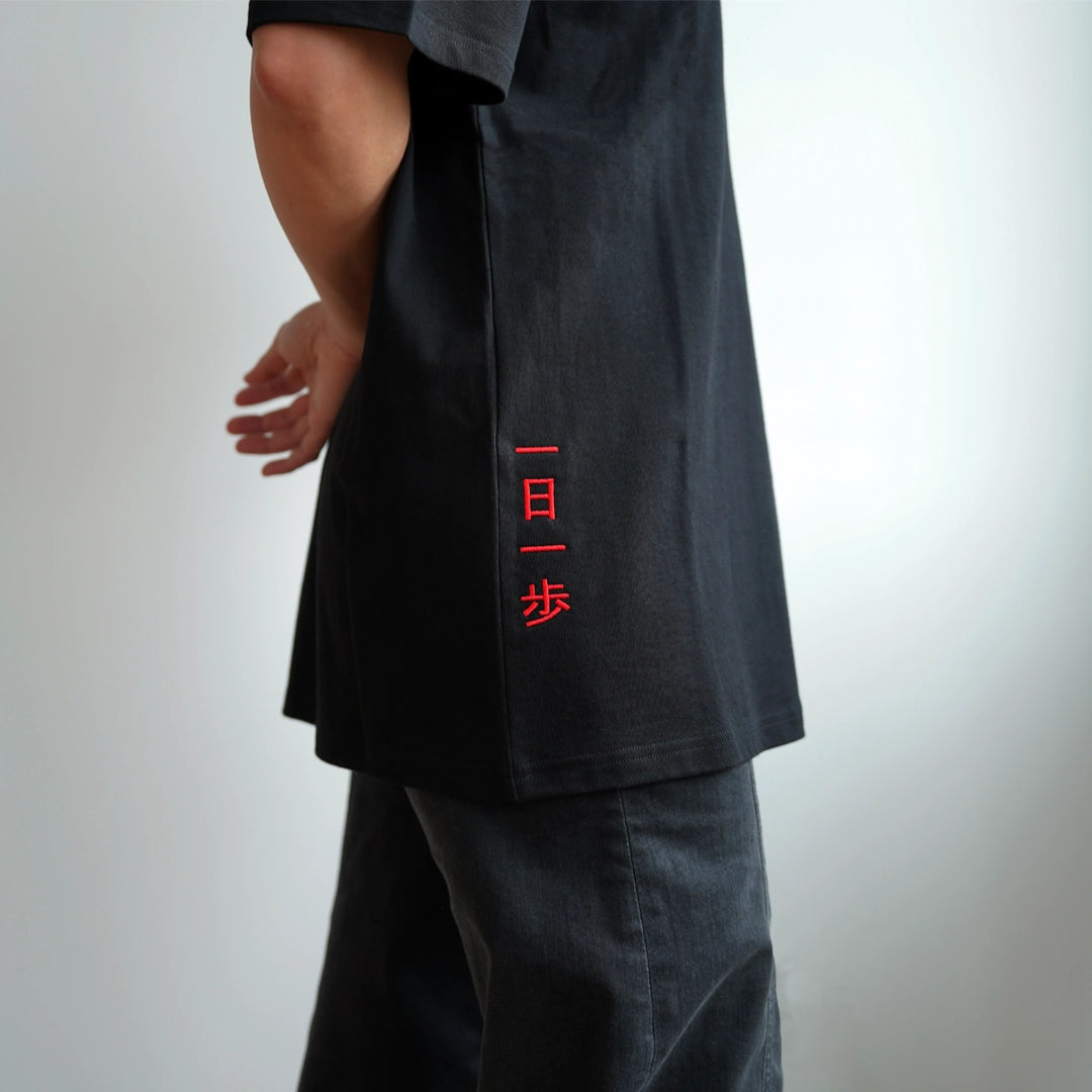 ODAAT Apparel black t-shirt featuring red Japanese embroidery ‘一日一歩’ meaning ‘One day, one step’—a minimalist design inspired by Japanese aesthetics and daily progress. Modeled on a person in black pants, reflecting intentional, resilient style.
