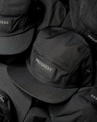 Close-up of stacked black performance caps with PROGRESS branding, highlighting material texture, stitching, and structured construction
