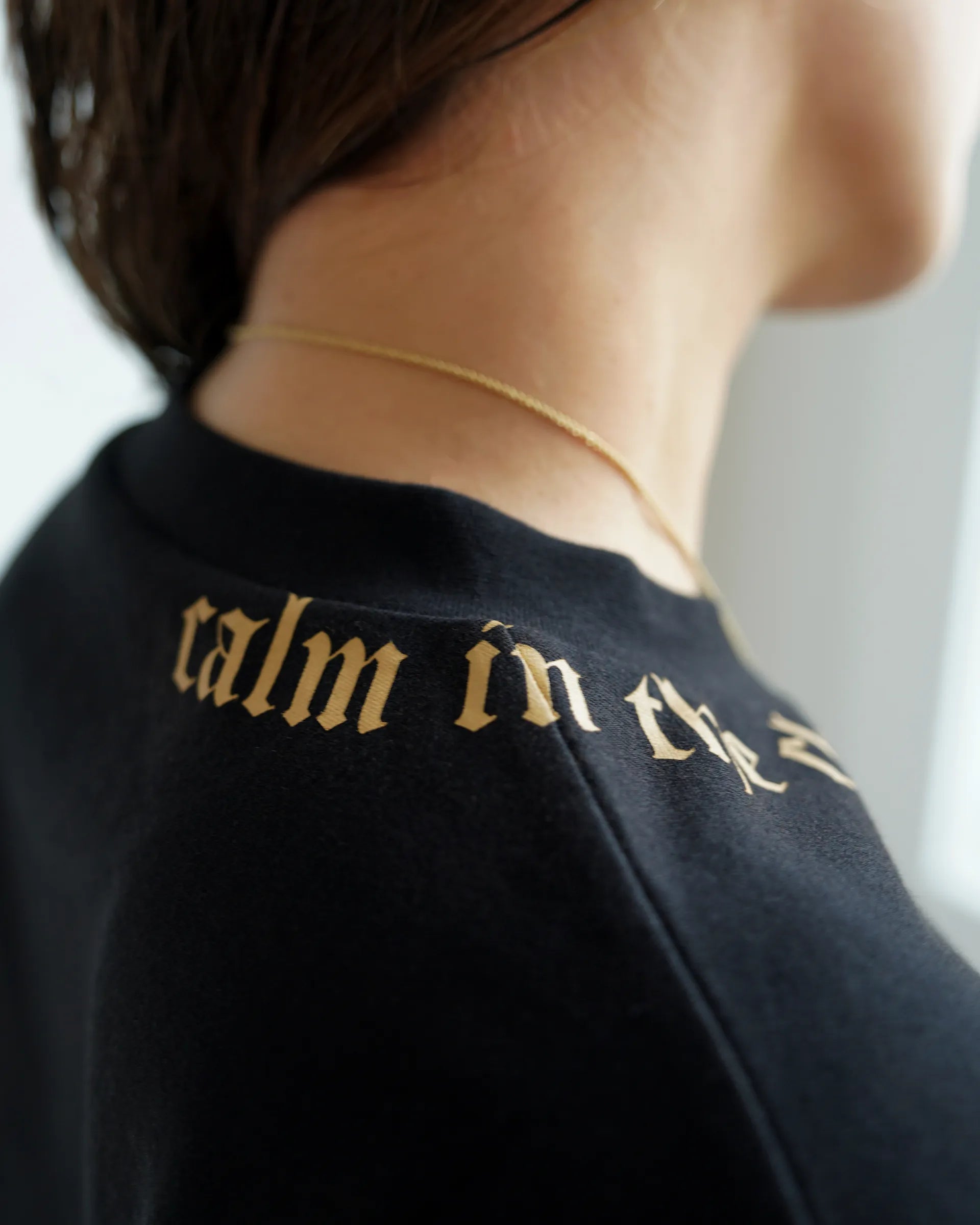 Close-up of Calm in the Chaos boxy cropped tee in black with gold neckline graphic