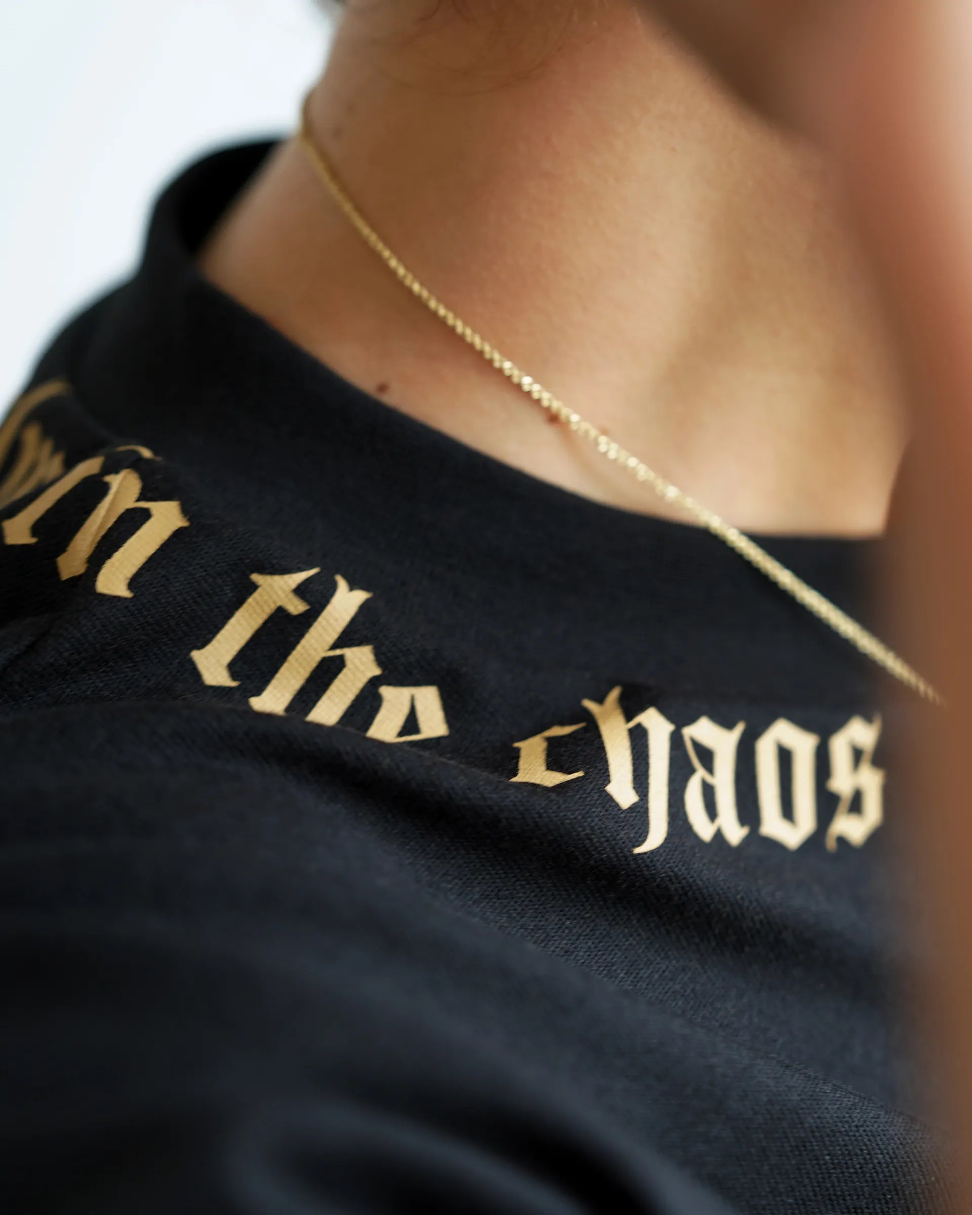 Calm in the Chaos boxy cropped tee in black with gold neckline graphic, angled close-up