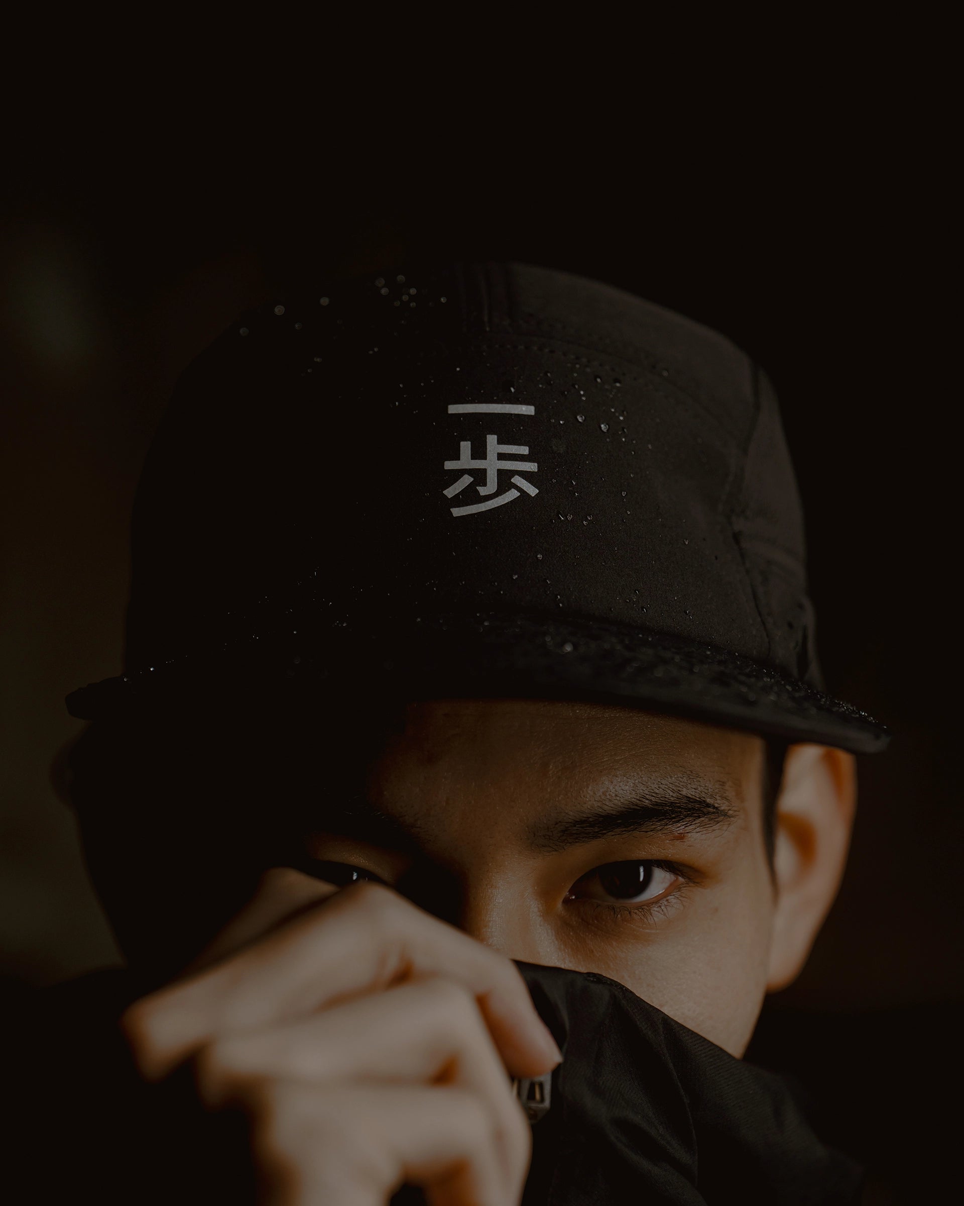 Man wearing a black KyoPace running cap with Kanji in low light, close-up portrait