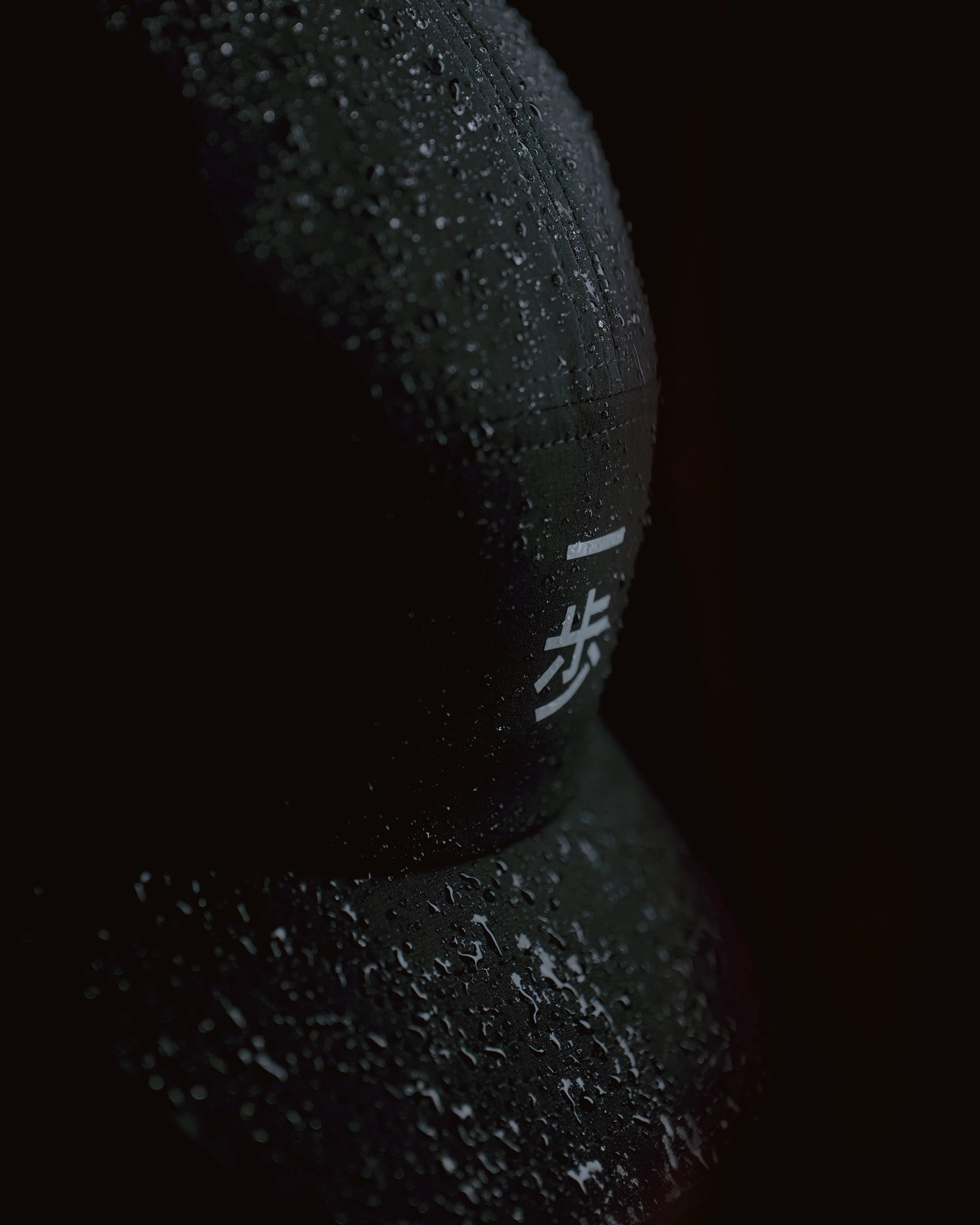 Black KyoPace running cap with crane logo, close-up detail with water droplets on fabric