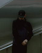 Man wearing a black KyoPace running cap with kanji mark on front in a moody indoor setting