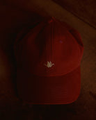 burgundy signature dad cap close-up showing curved brim and panel construction, soft cotton fabric with crane embroidery, minimal product detail shot with warm low light background