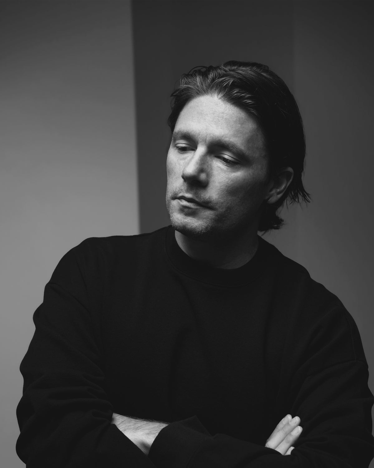 Black and white portrait of ODAAT founder Jeremy Webster in a dark crewneck, arms folded, looking down, against a plain wall.