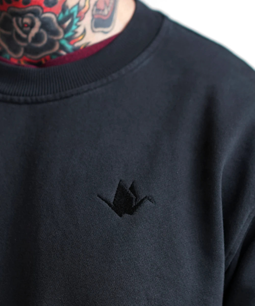 ODAAT black crewneck sweatshirt with tonal origami crane embroidery, worn by tattooed model — front detail.
