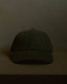olive signature dad cap front view with curved brim, structured crown and centered crane embroidery, minimal product shot on neutral surface with soft warm lighting