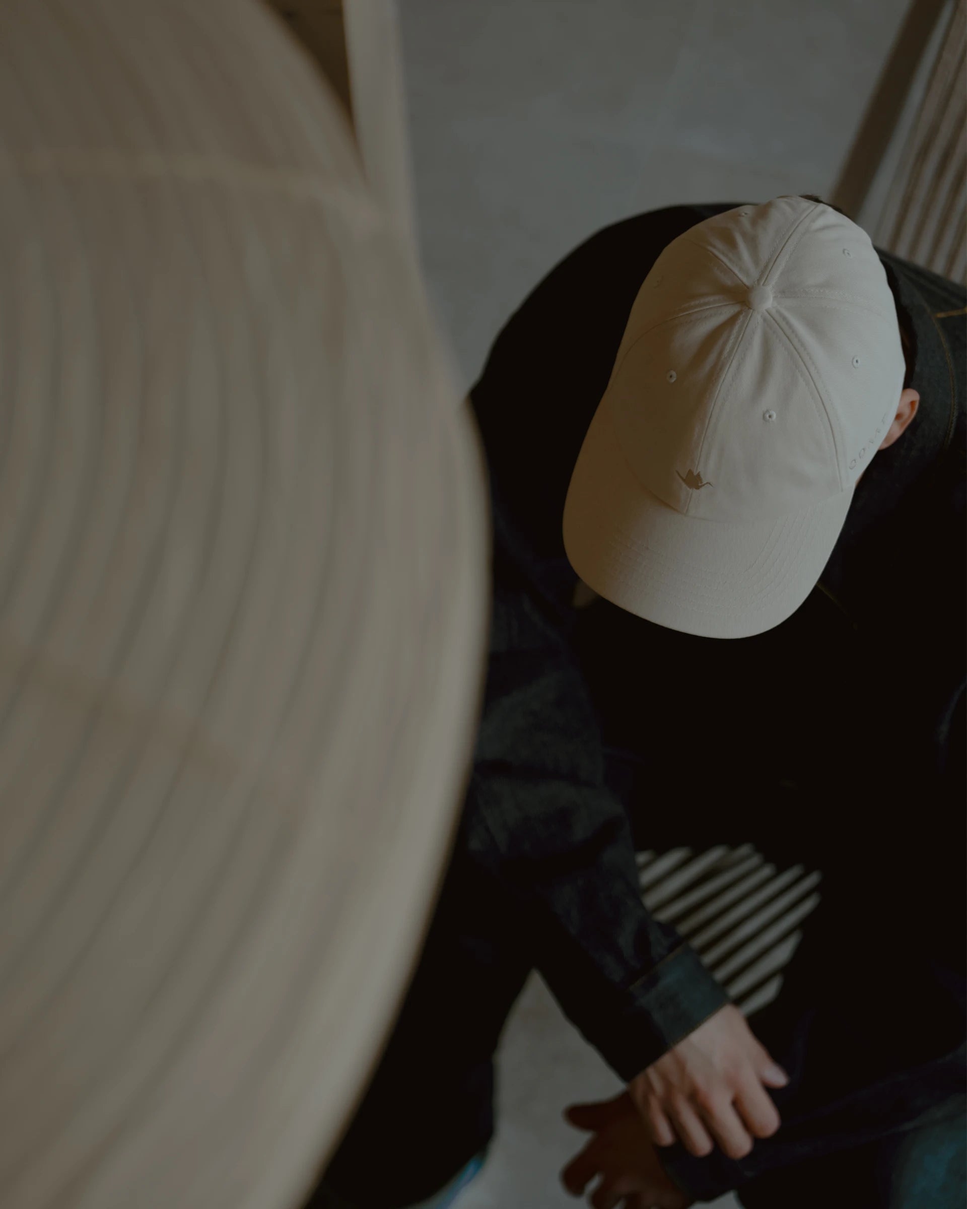 rice paper signature dad cap worn by model, top-down lifestyle angle showing curved brim and crown shape, soft cotton fabric with subtle crane embroidery, neutral indoor setting with architectural lines