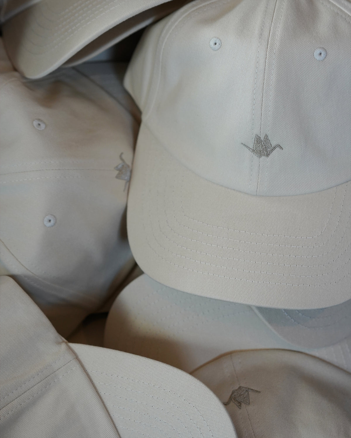 ODAAT Icon Cap in Rice Paper, stacked caps showing the brushed cotton, curved brim and tonal Orizuru embroidery.