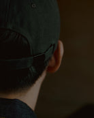 washed black signature dad cap rear view showing self-fabric strap and metal adjuster, soft cotton construction with clean stitching, minimal design detail on warm blurred background