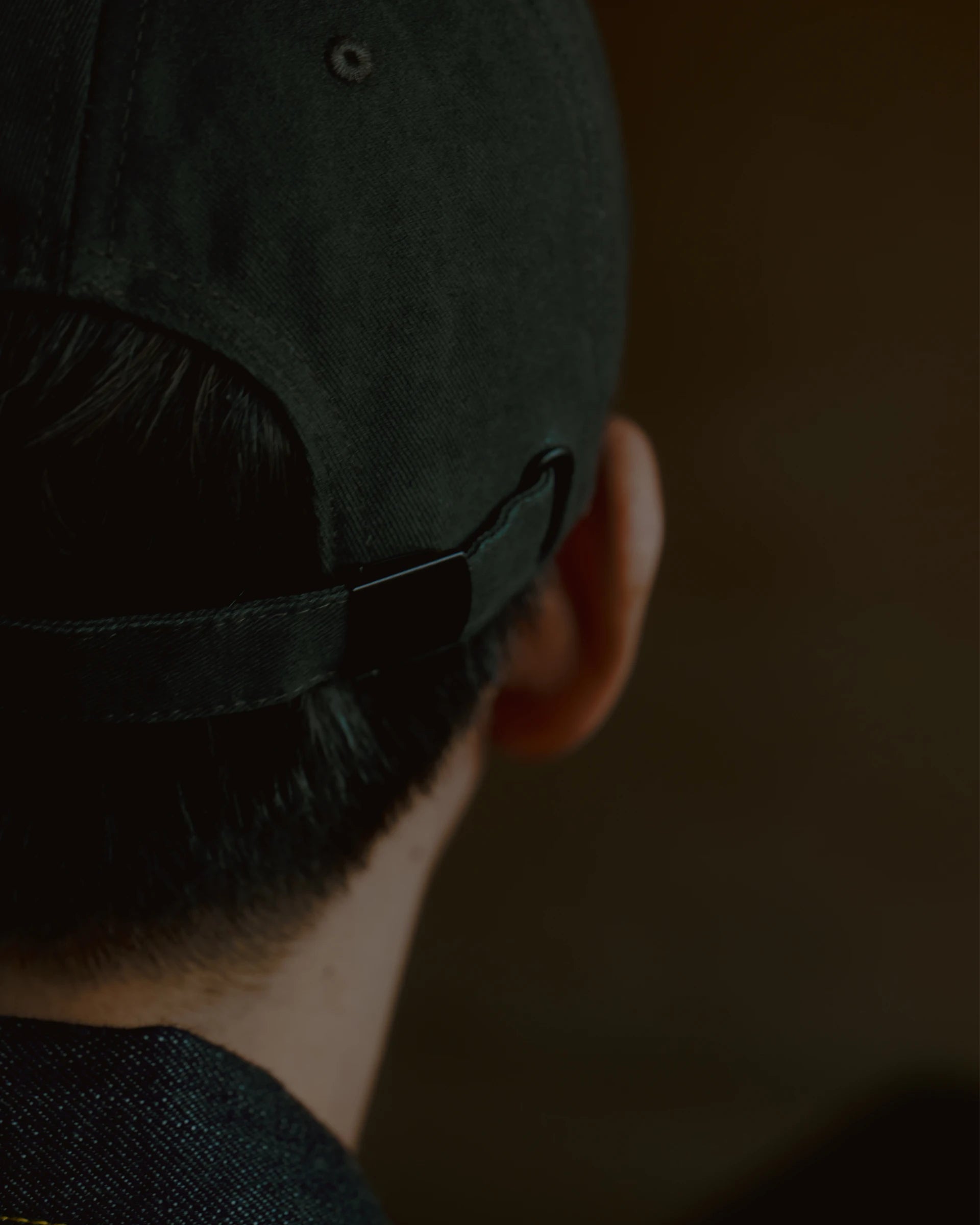 washed black signature dad cap rear view showing self-fabric strap and metal adjuster, soft cotton construction with clean stitching, minimal design detail on warm blurred background